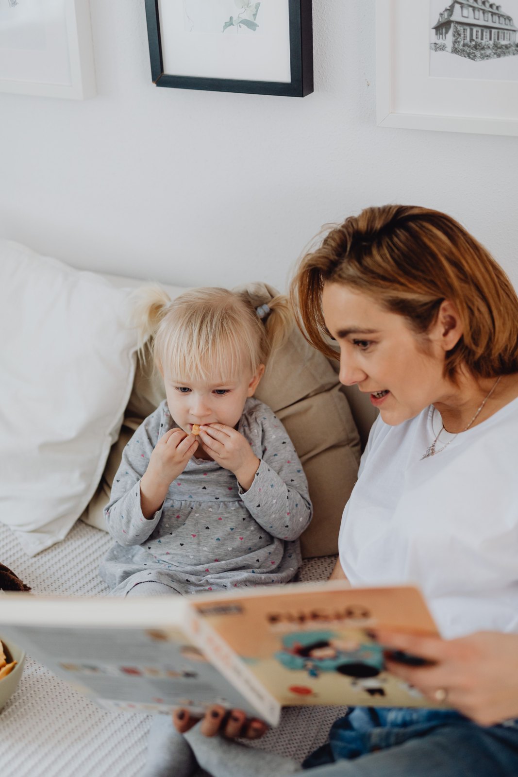 An adult and a child looking at a book on a sofa